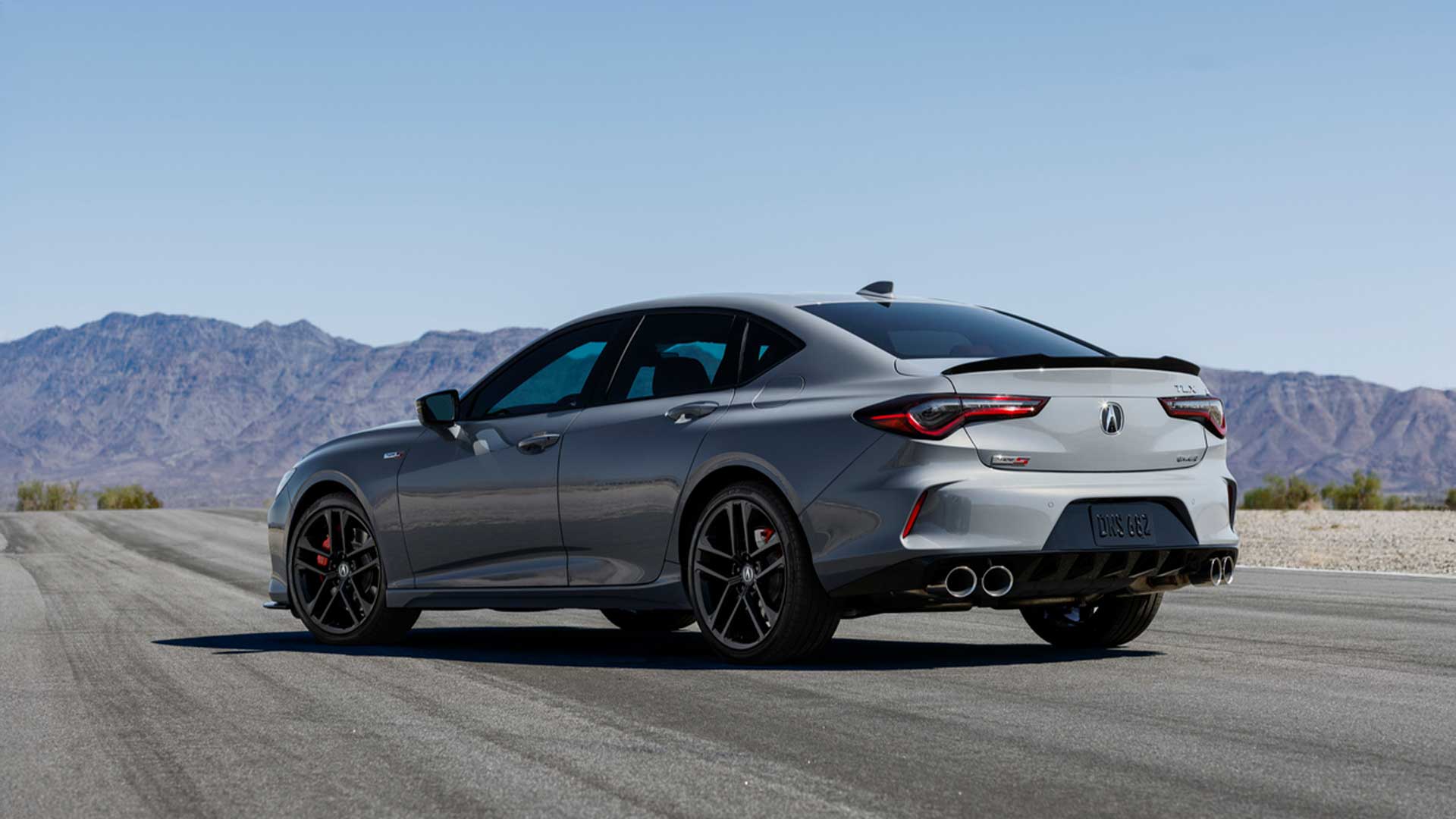 rear three-quarter view of grayt acura tlx type s showcasing quad exhaust tips and performance tires against mountain backdrop